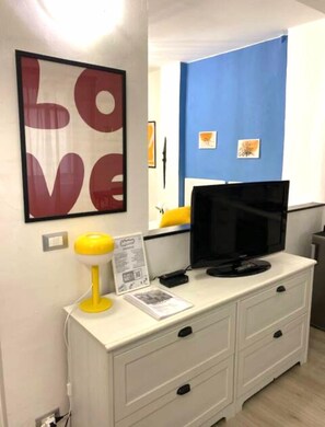 A room with a white dresser, a yellow lamp, a black TV on top, a framed 'LOVE' sign, and a blue accent wall. - La Piazzetta-your retreat just a few meters from the aquarium  (Genova)