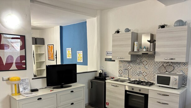 Une cuisine moderne avec des meubles blancs, un four à micro-ondes encastré, une cuisinière à gaz et un petit réfrigérateur.