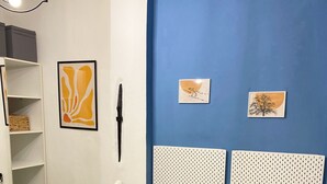 Un lit avec une couvre-lit à motifs, deux coussins de couleur moutarde, un plaid noir, une tête de lit blanche et un mur orné de deux tableaux encadrés.