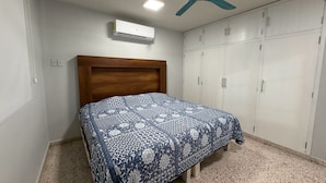 Une chambre à coucher comprenant un lit, un ventilateur de plafond, un climatiseur et une armoire.