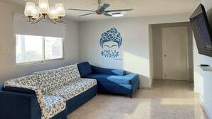 Un salon avec un canapé à motifs, un ventilateur de plafond, un téléviseur fixé au mur et un adhésif décoratif sur le mur.
