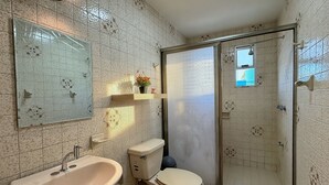 Une salle de bain comprenant un lavabo, des toilettes et un espace douche, avec des murs carrelés et un miroir.