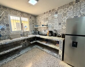 A kitchen with patterned tiles, a stainless steel refrigerator, a microwave, a coffee maker, and a water dispenser.