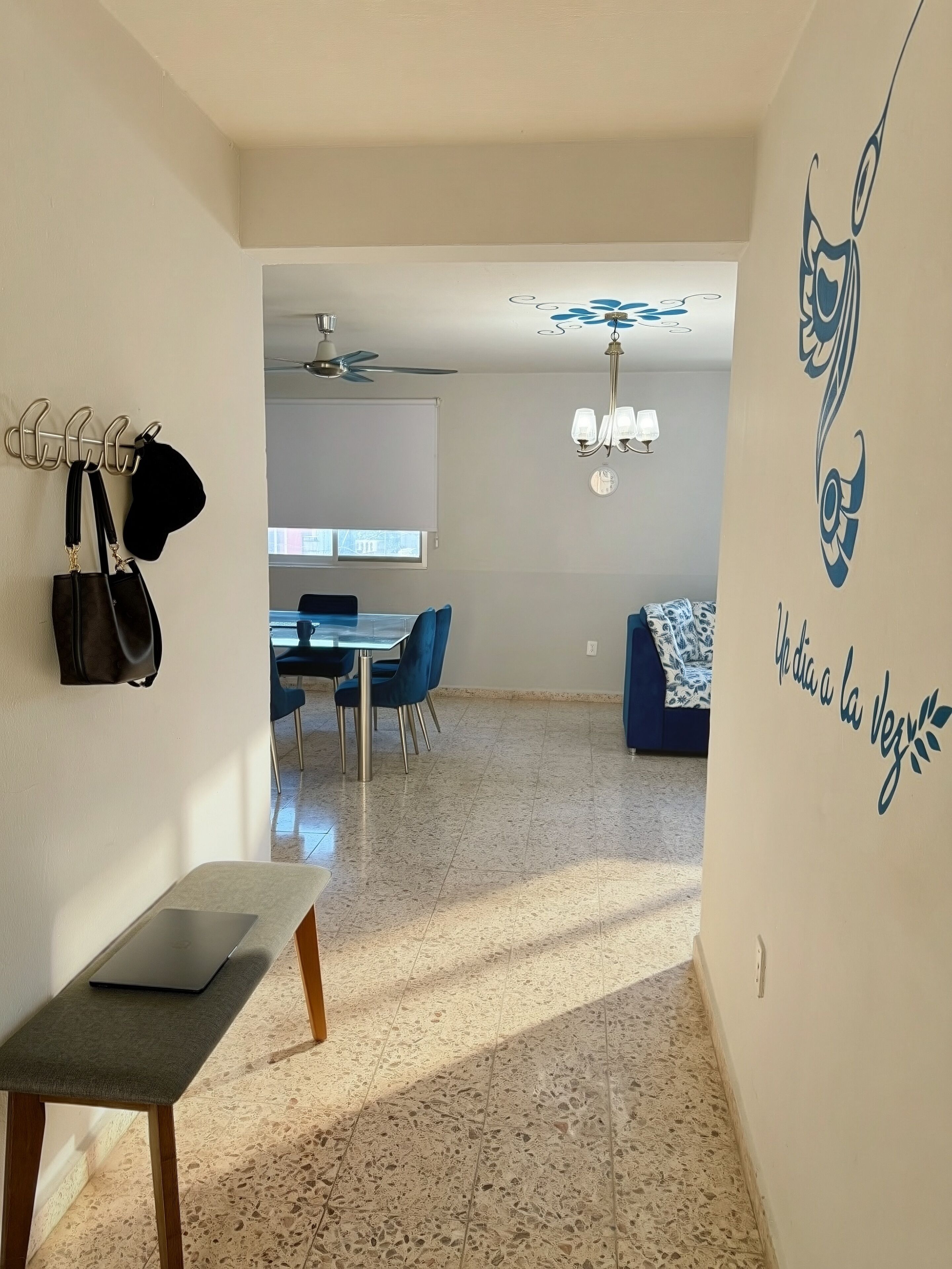 A modern living room with a dining area, a laptop on a bench, and a wall with a decorative design.