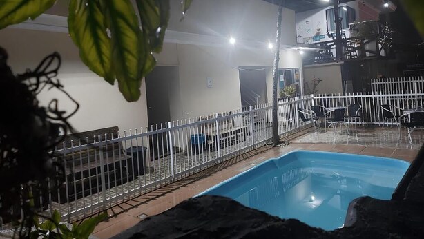 An indoor swimming pool area with a white fence, a pool, and a building in the background. - Pousada Ilha do Itacolomi (Penha)