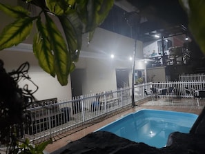 An indoor swimming pool area with a white fence, a pool, and a building in the background.