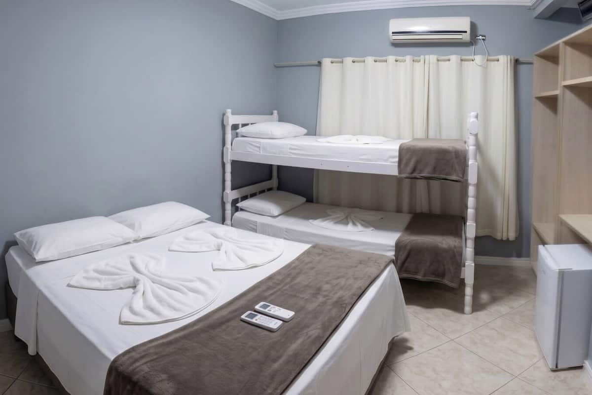 Una habitación con dos camas, una mesita de noche con un control remoto, aire acondicionado en la pared y una cortina.