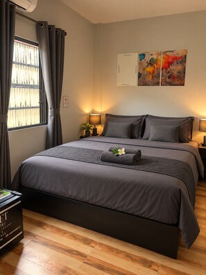 Un dormitorio ordenado con una cama grande, una mesita de noche con lámpara y una ventana con cortinas.