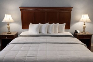 Ein Hotelzimmer mit einem großen Bett, einem Holz-Kopfteil, weißer Bettwäsche, zwei Nachttischen mit Lampen und einem Telefon auf einem der Tische.
