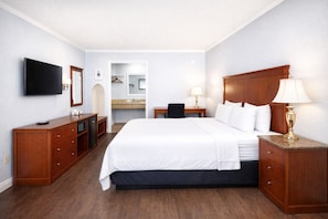 Ein Hotelzimmer mit Bett, Fernseher, Schreibtisch, Stuhl, Kommode und Spiegel.