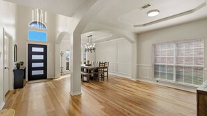 A spacious interior with a wooden floor, a dining area with a table and chairs, and a large window with blinds.