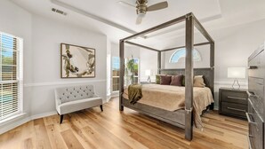 A four-poster bed with a wooden frame, a tufted bench, a bedside table, and a wall-mounted lamp.