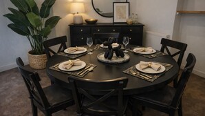 Una mesa de comedor redonda con sillas negras, un mueble negro con tiradores dorados, una planta en maceta y un espejo fijado a la pared.