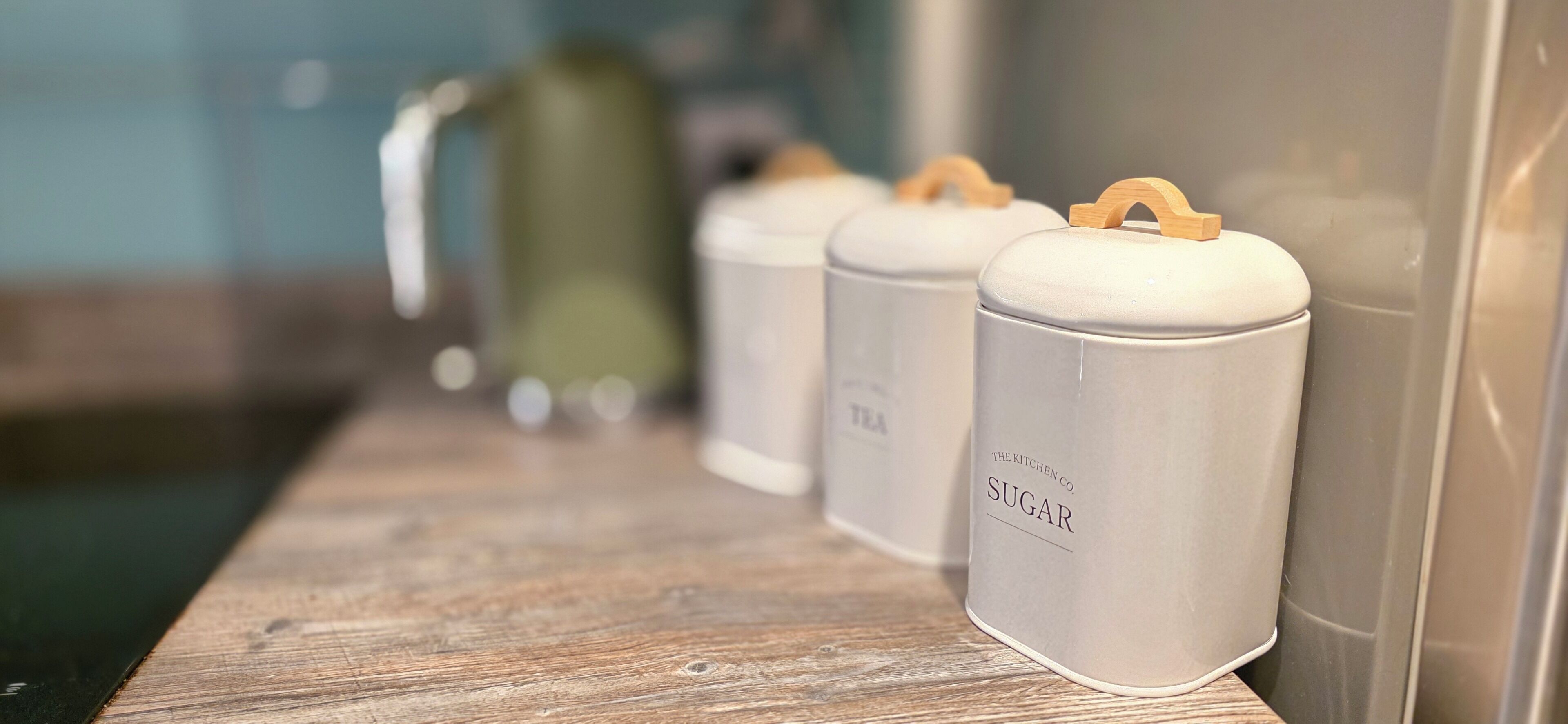 Four white containers with wooden handles on a wooden shelf.
