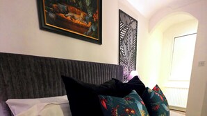 Una habitación de hotel con cama, almohadas, cabecero, un cuadro enmarcado y un panel decorativo en la pared.