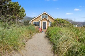 A coastal house with a sandy pathway leading to the entrance, surrounded by tall grass and trees. - Spacious Group Getaway w/ Main House + Private Studio, Sleeps 10, Ideal for Families (Rockaway Beach)
