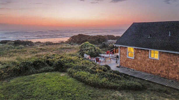 Una casa costera con terraza, vista al océano y zona verde.