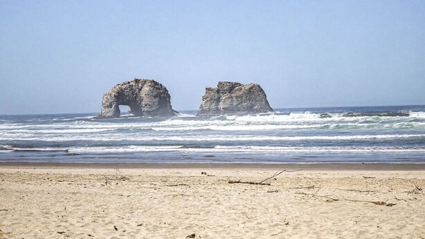 Una spiaggia con due formazioni rocciose in mare.