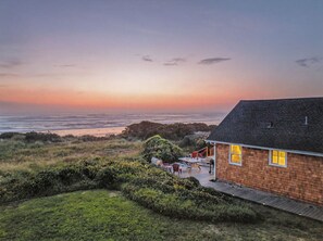 Uma casa à beira-mar com varanda, vista para o oceano e área gramada.