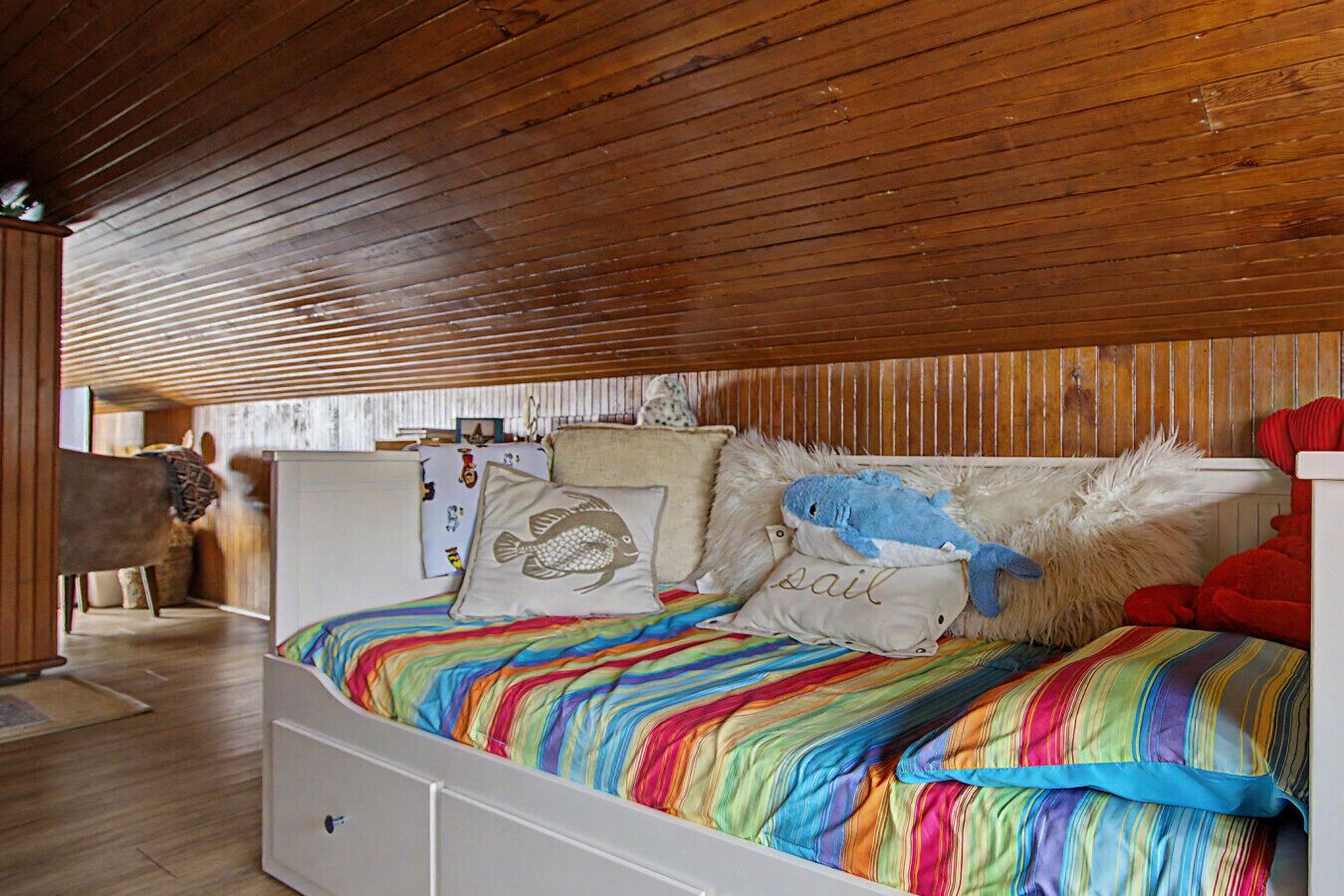 A bedroom with a wooden ceiling, a bed with colorful bedding, and a plush shark toy.