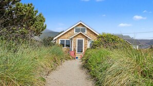 A coastal house with a sandy pathway leading to the entrance, surrounded by tall grass and trees. - Beachfront retreat with hot tub | Dog-friendly (Rockaway Beach)