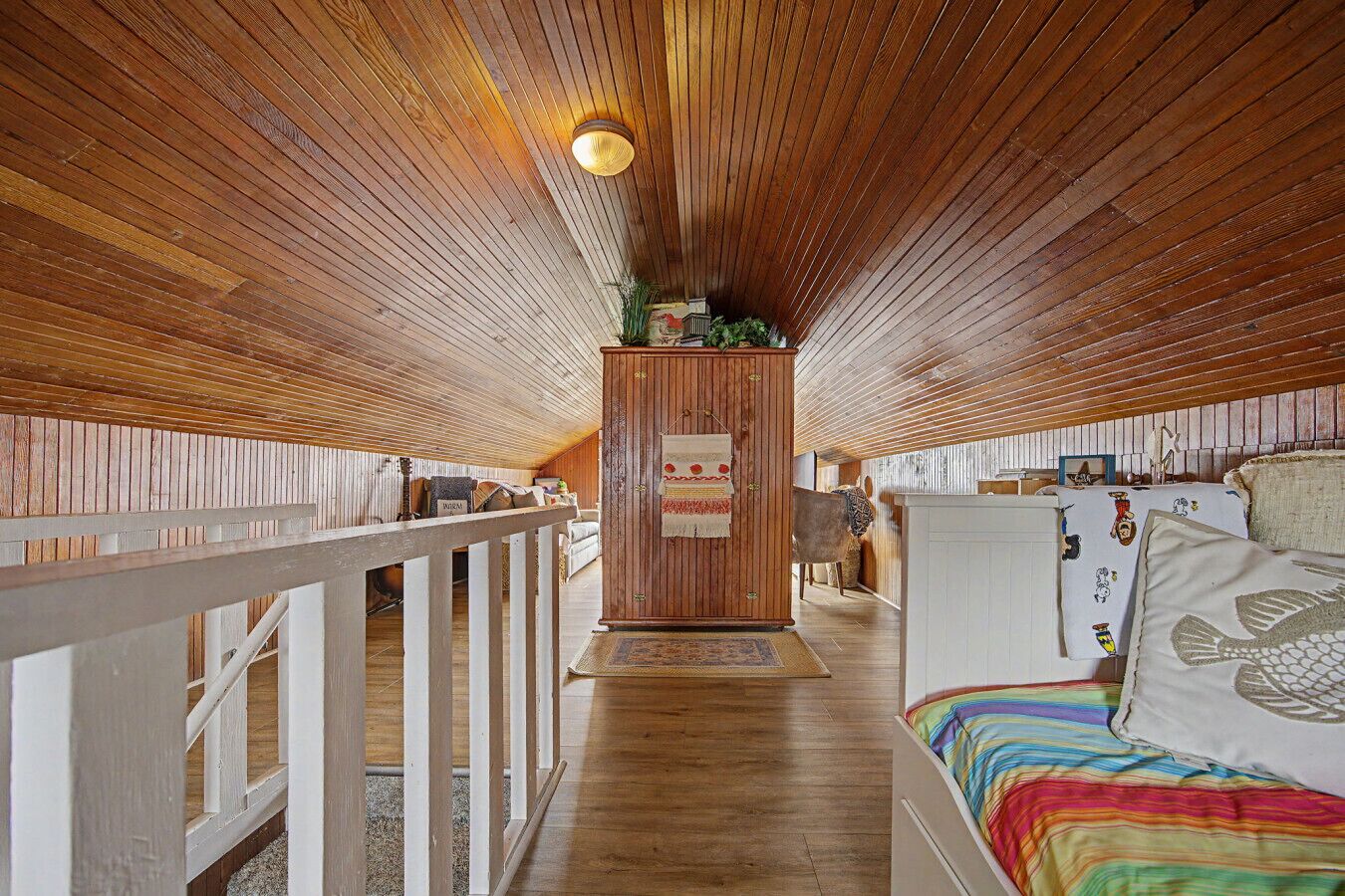 A wooden interior with a bunk bed, a wooden cabinet, and a white railing.