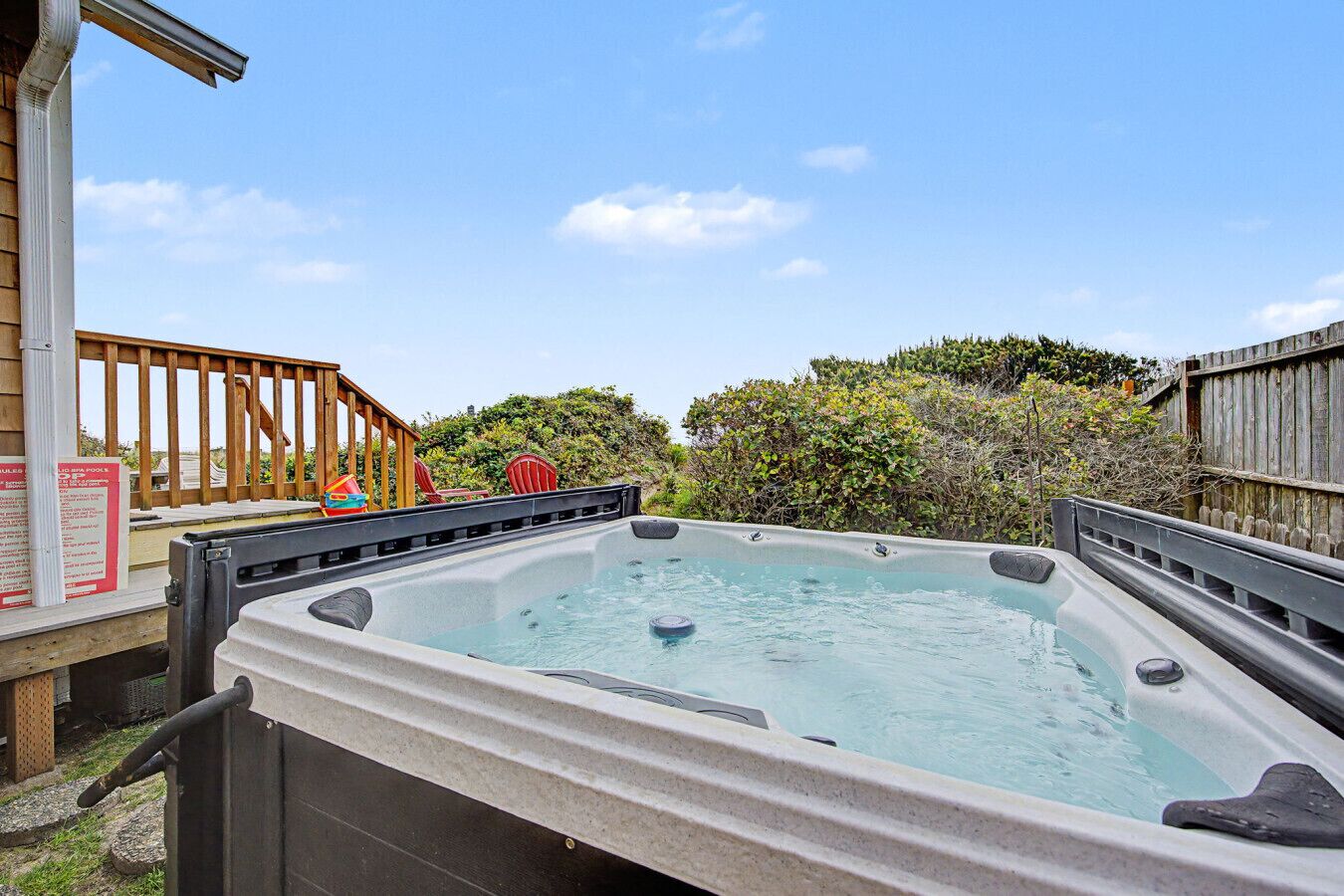 Un bain à remous installé à l’extérieur, avec une terrasse en bois, une clôture en bois et de la verdure en arrière-plan.