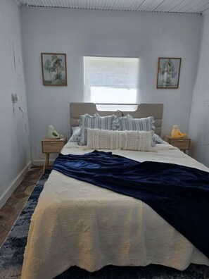 A bedroom with a bed, two nightstands, a window, and two wall-mounted paintings. - Cozy Private Cottage Close To Downtown and Beaches (West Palm Beach)