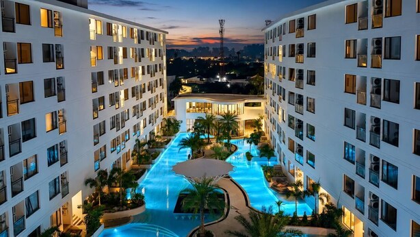 Un hôtel à étages, doté d’une piscine centrale et offrant une vue sur les toits de la ville au crépuscule.