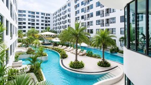 A modern hotel with a central swimming pool surrounded by palm trees and lounge chairs.