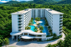 A multi-story hotel with a central swimming pool, surrounded by lush greenery and palm trees. - Stylish Capri residense BangTao Beach (Choeng Thale)