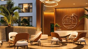 A modern hotel lobby with a reception desk, seating area, and a view of the building's exterior.