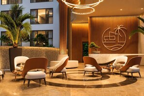 A modern hotel lobby with a reception desk, seating area, and a view of the building's exterior. - Stylish Capri residense BangTao Beach (Choeng Thale)