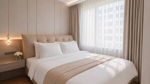 A modern hotel room with a large bed, a bedside table with a lamp, and a view of the city through sheer curtains.