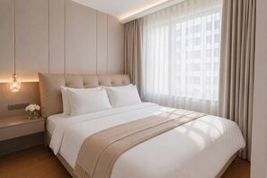 A modern hotel room with a large bed, a bedside table with a lamp, and a view of the city through sheer curtains. - Stylish Capri residense BangTao Beach (Choeng Thale)