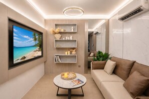 A modern living room with a flat-screen TV, a round coffee table, a sofa, and built-in shelving with decorative items. - Stylish Capri residense BangTao Beach (Choeng Thale)