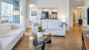 A modern living room with a glass coffee table, white sofas, and a view of the kitchen. - Fantastic 1 bed and den in Yaletown across from the world famous Seawall! (Vancouver)