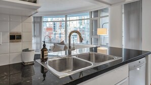 A modern kitchen with a double sink, a bottle of hand sanitizer, and a view of the city through large windows. - Fantastic 1 bed and den in Yaletown across from the world famous Seawall! (Vancouver)