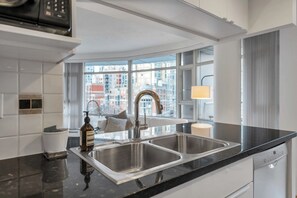 Eine moderne Küche mit einer doppelten Spüle, einer Handdesinfektionsmittel-Flasche und Blick auf die Stadt durch große Fenster.