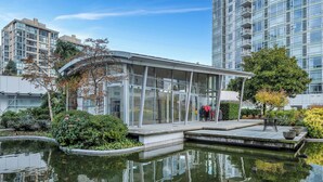 A modern building with a glass facade, a small outdoor seating area, and a reflective water feature. - Fantastic 1 bed and den in Yaletown across from the world famous Seawall! (Vancouver)