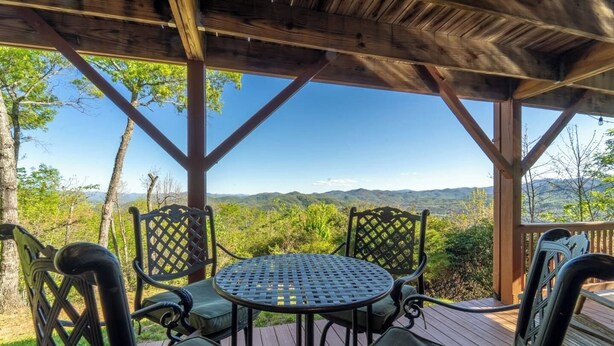 Un espacio de estar techado al aire libre con mesa y sillas, con vistas a un paisaje montañoso.