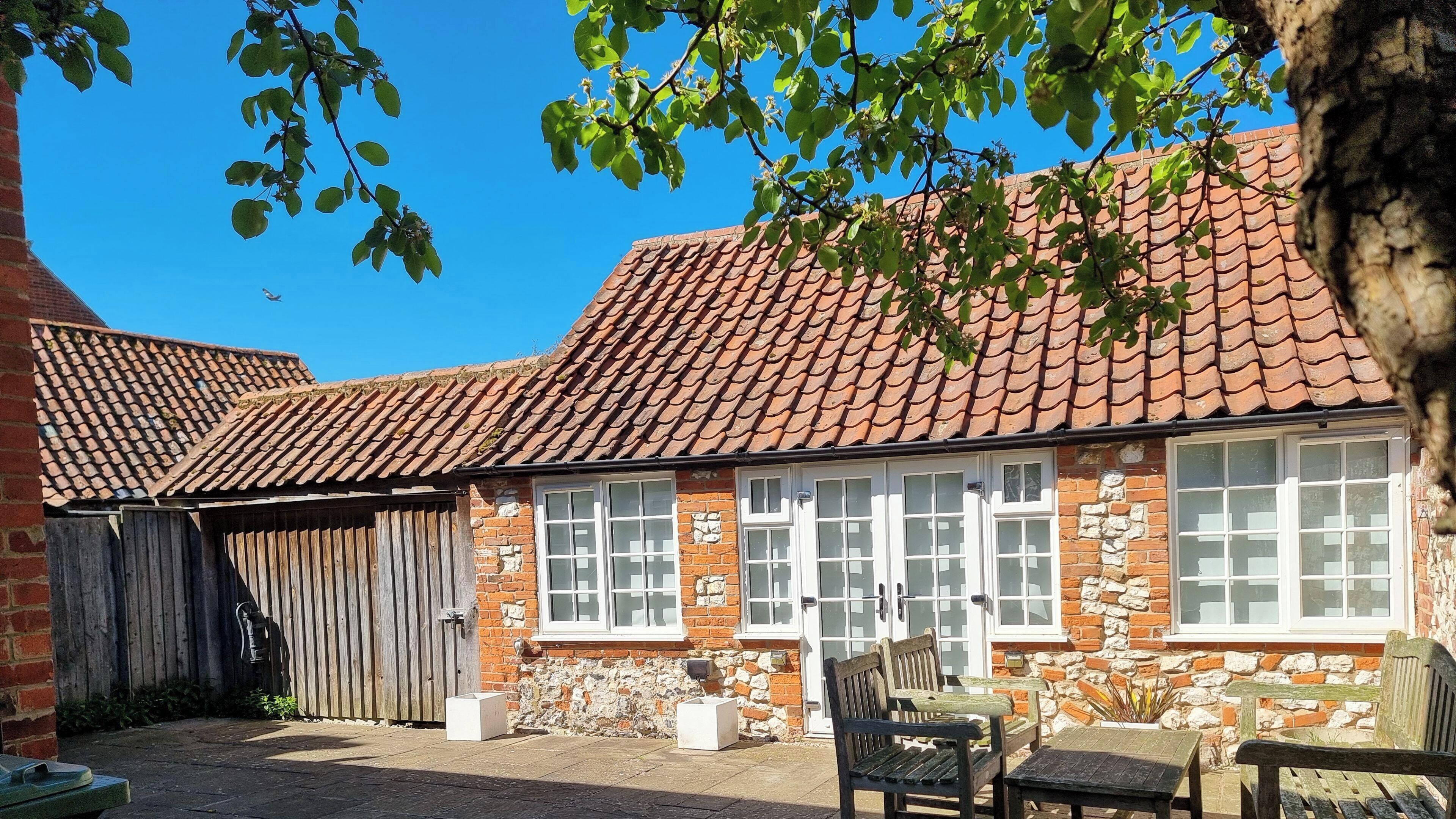 A brick building with a tiled roof, stone walls, and a wooden fence.