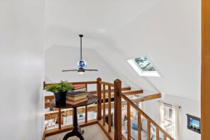 Un escalier avec des rampes en bois, un ventilateur de plafond et un puits de lumière.