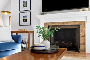 Un salon avec un canapé bleu, une table basse en bois, une cheminée et des tableaux encadrés accrochés au mur.