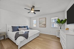 A bedroom with a bed, bedside tables, a ceiling fan, artwork, and a window.