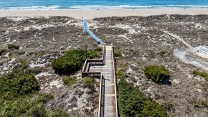 A beach with a wooden boardwalk leading to a structure with a blue roof. - Golden Hour Getaway | Sleeps 12 | Pool + Beach (Atlantic Beach)
