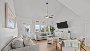 A modern living room with a sofa, armchairs, a TV, and a ceiling fan. - Golden Hour Getaway | Sleeps 12 | Pool + Beach (Atlantic Beach)