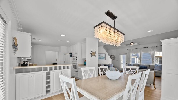 A modern kitchen with white cabinetry, a wooden dining table, and a chandelier. - Golden Hour Getaway | Sleeps 12 | Pool + Beach (Atlantic Beach)