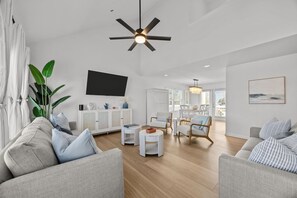 A spacious living room with a ceiling fan, a flat-screen TV, a dining area, and a view of the outdoors.