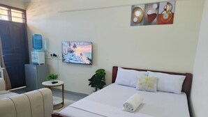 Hotellihuone, jossa on sänky, työpöytä, tuoli, juomavesiautomaatti, televisio ja taulu seinällä.